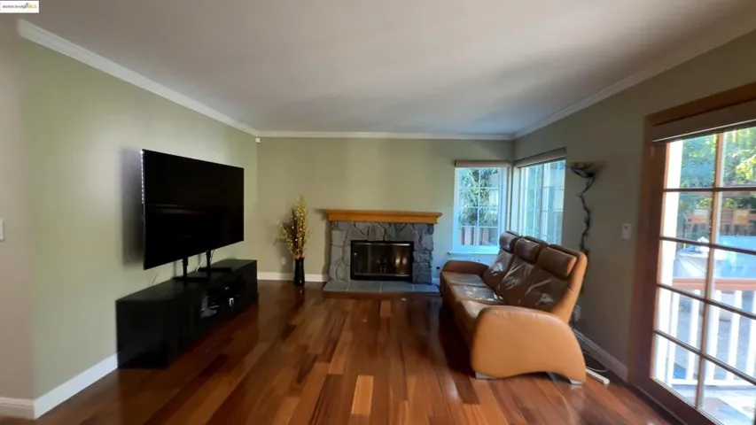 Living room with a stone fireplace, crown molding, and dark wood-type flooring