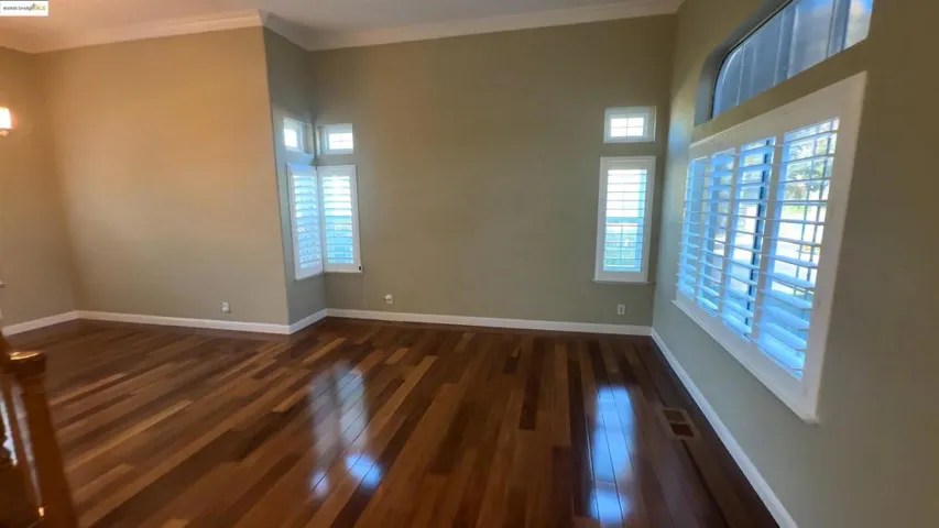 Empty room with ornamental molding, dark wood-style floors, and a chandelier