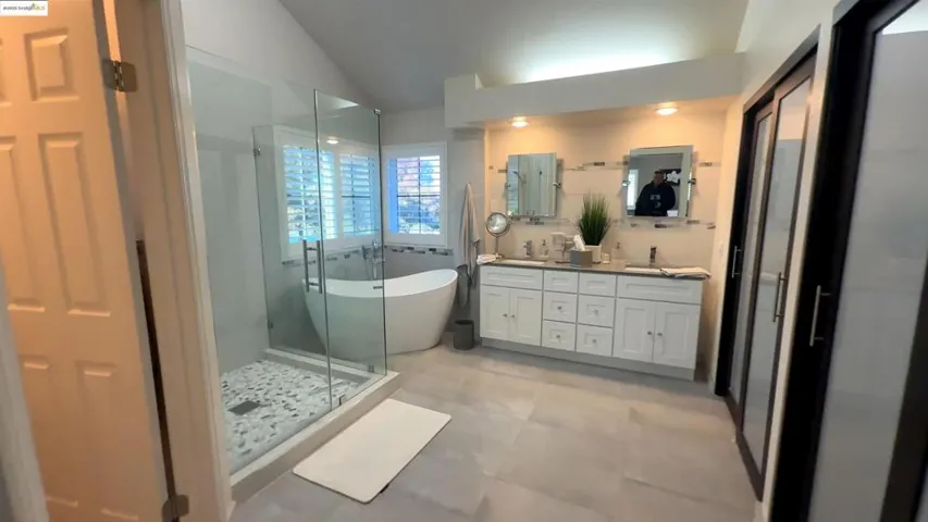 Full bath with double vanity, a freestanding tub, a stall shower, and lofted ceiling