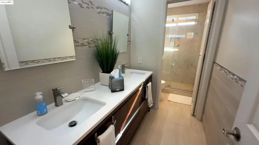 Full bathroom featuring a shower stall, double vanity, tasteful backsplash, and light tile patterned floors