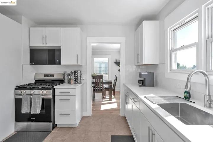Kitchen featuring white cabinetry, stainless steel gas stove, black microwave, decorative backsplash, and light stone counters