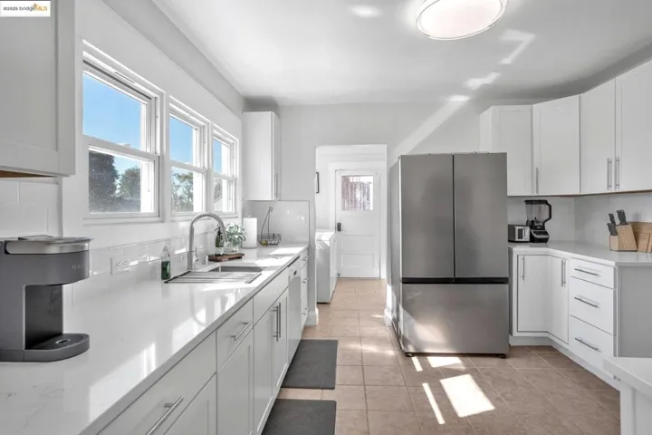 Kitchen featuring tasteful backsplash, freestanding refrigerator, white cabinets, light stone countertops, and light tile patterned floors