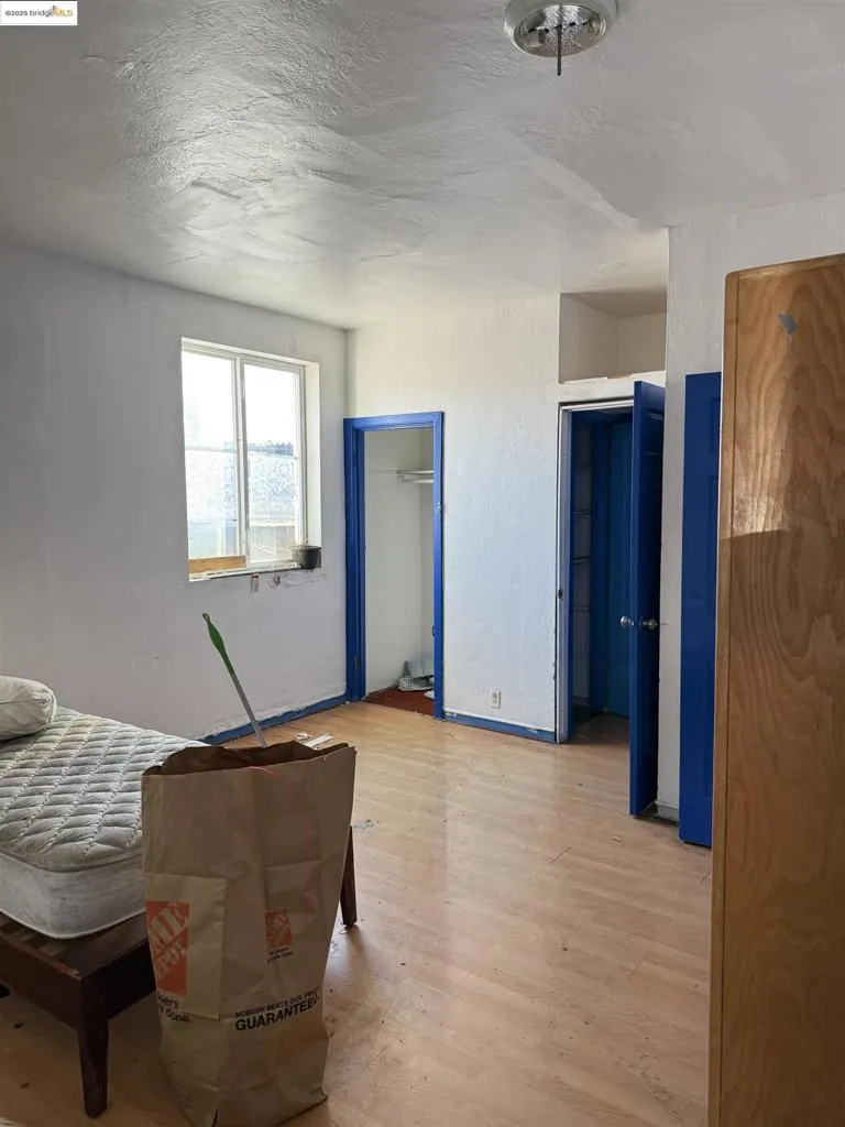 Bedroom featuring light wood-style flooring, a textured ceiling, multiple closets, and a textured wall