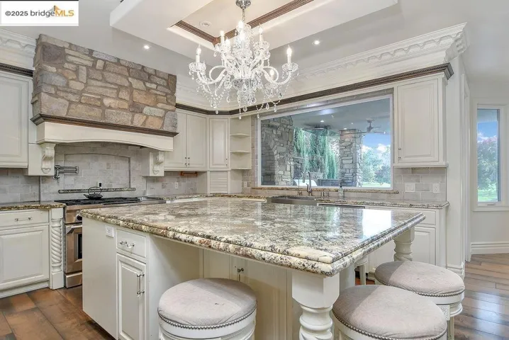 Kitchen with dark wood-type flooring, light stone counters, backsplash, and white cabinetry
