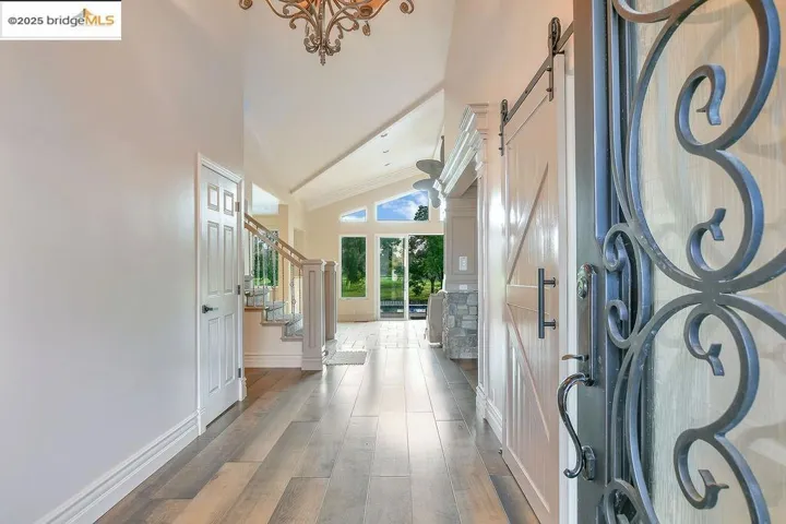 Entryway with a barn door, stairway, wood finished floors, high vaulted ceiling, and a chandelier