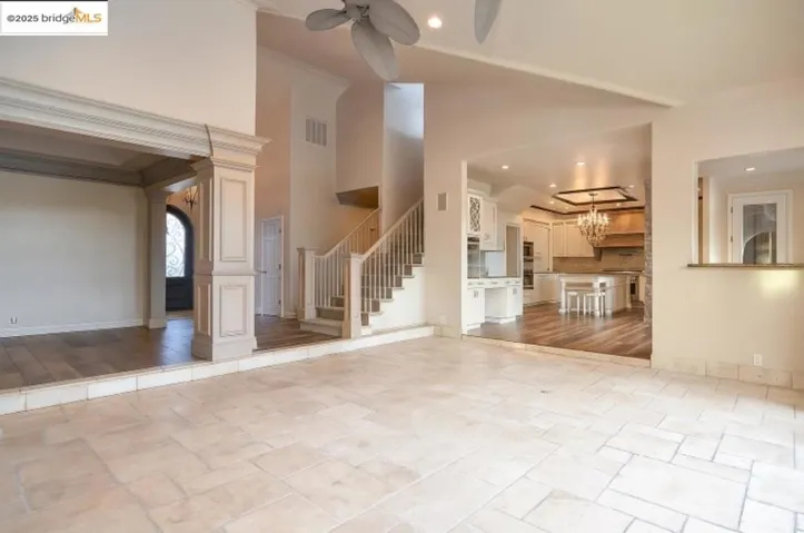 Unfurnished living room with stone tile flooring, ceiling fan, stairway, a chandelier, and recessed lighting