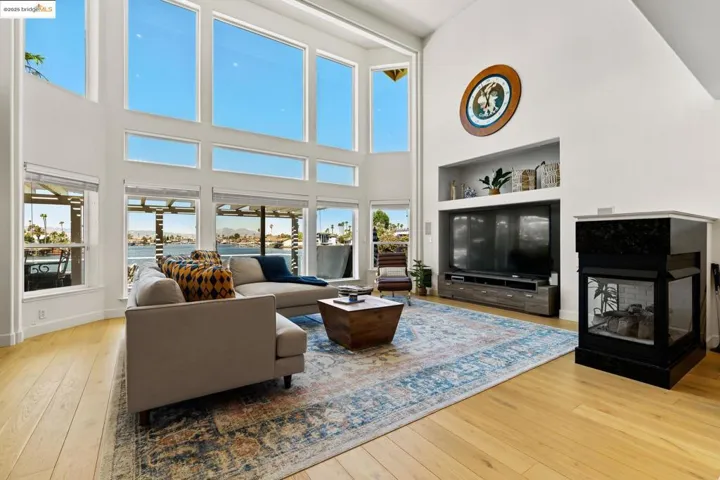 Living room featuring plenty of natural light, light wood finished floors, a multi sided fireplace, and a towering ceiling