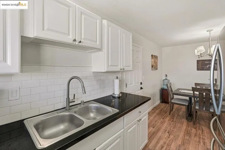 Kitchen with dark countertops, white cabinetry, decorative backsplash, stainless steel fridge, and dark wood-style flooring