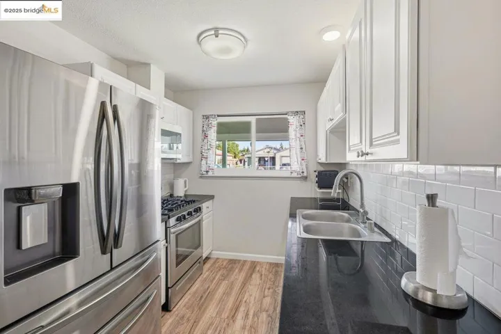 Kitchen with stainless steel appliances, white cabinetry, light wood-style flooring, dark countertops, and a textured ceiling