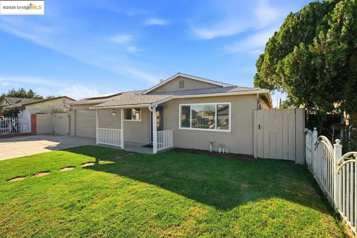 View of front facade with stucco siding, driveway, an attached garage, and a gate