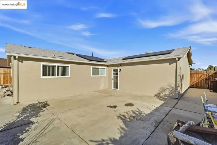 Rear view of house with a fenced backyard, a patio, stucco siding, roof mounted solar panels, and a shingled roof