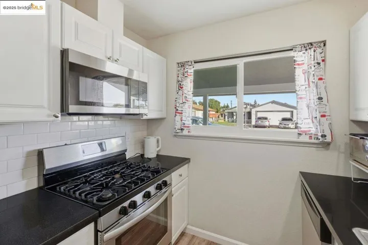 Kitchen with appliances with stainless steel finishes, white cabinetry, backsplash, and light wood-style flooring