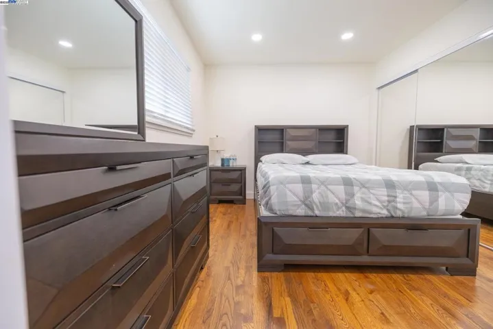 Elegant master suite featuring rich hardwood floors, a modern bedroom set, mirrored wardrobe, and a serene layout. The attached spa-inspired bath offers a quartz vanity, matte-black fixtures, and a beautifully tiled glass shower. Furniture Included.