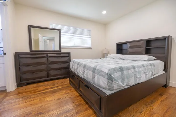 Elegant master suite featuring rich hardwood floors, a modern bedroom set, mirrored wardrobe, and a serene layout. The attached spa-inspired bath offers a quartz vanity, matte-black fixtures, and a beautifully tiled glass shower. Furniture Included.