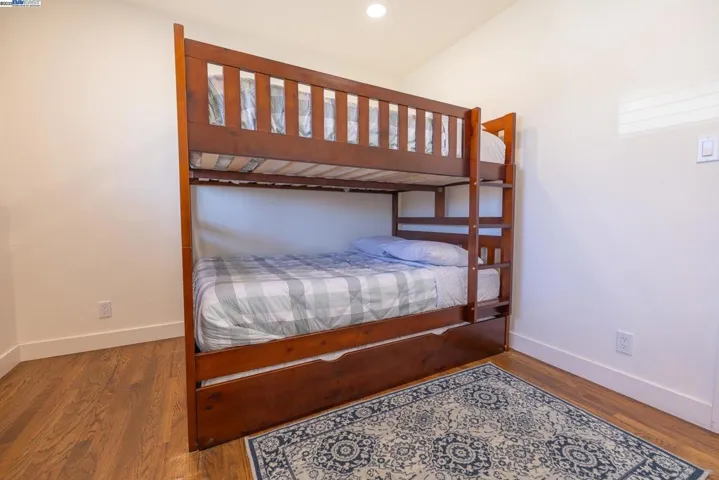 Cozy and well-kept bedroom featuring hardwood floors, recessed lighting, and a sturdy bunk-bed setup ideal for kids or guests. Includes a classic nightstand and area rug that add comfort and character. Furniture Included.