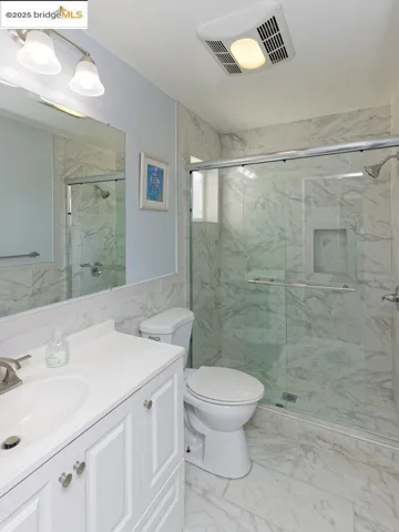Full bath with vanity, light marble finish floors, tile walls, a marble finish shower, and wainscoting
