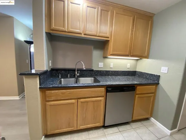Kitchen with brown cabinets, dishwasher, dark stone countertops, and light tile patterned floors