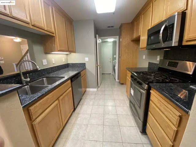 Kitchen with appliances with stainless steel finishes, dark stone counters, light tile patterned floors, and brown cabinets