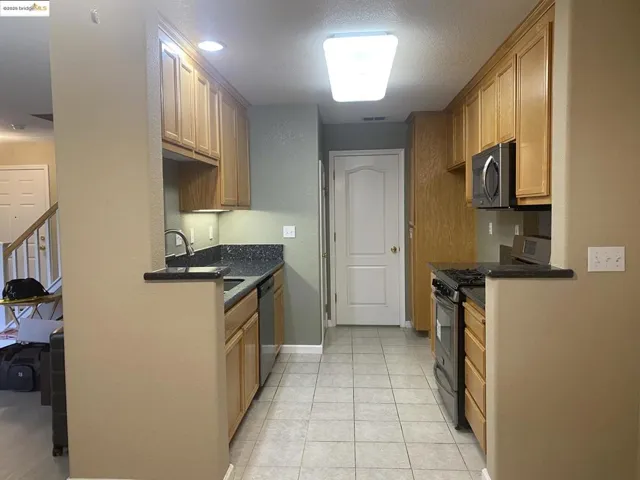 Kitchen with stainless steel appliances, dark stone counters, light tile patterned floors, and a textured ceiling