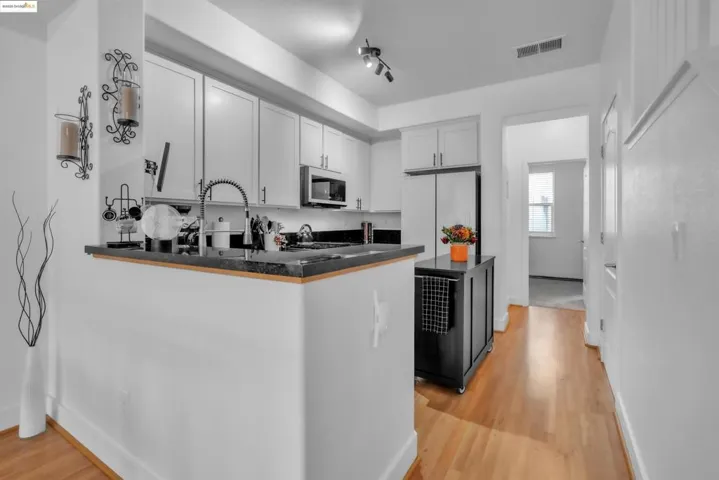 Kitchen with dark countertops, white cabinets, light wood finished floors, a peninsula, and freestanding refrigerator