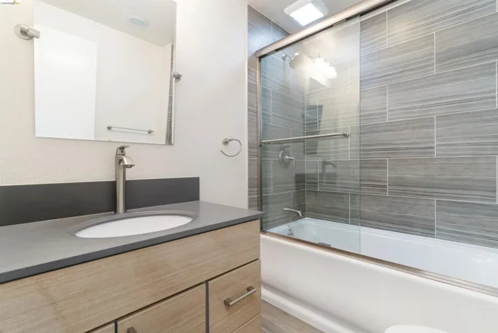 Full bathroom with vanity, enclosed tub / shower combo, and a textured wall