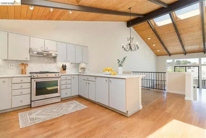 Kitchen featuring a high wooden beamed ceiling, gas range, a peninsula, decorative backsplash, and light wood finished floors