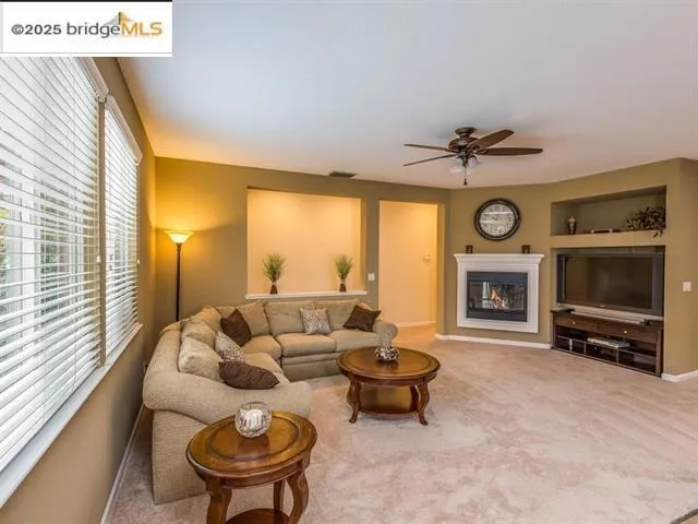 Carpeted living area with a glass covered fireplace, ceiling fan, and built in shelves