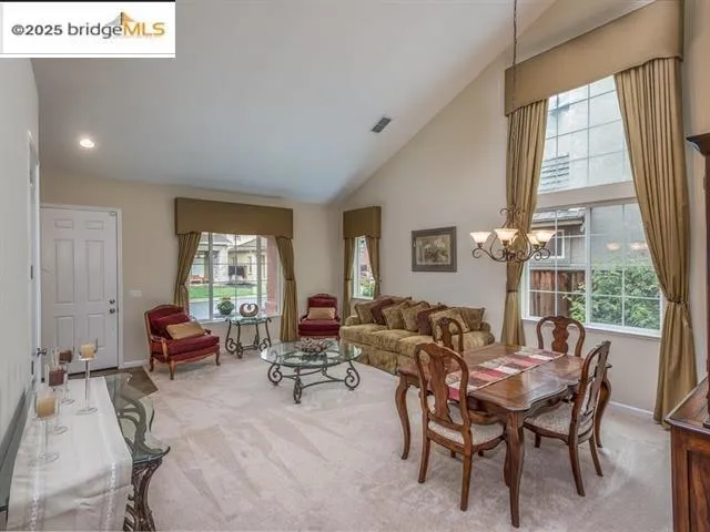 Dining space with carpet, high vaulted ceiling, healthy amount of natural light, and a chandelier
