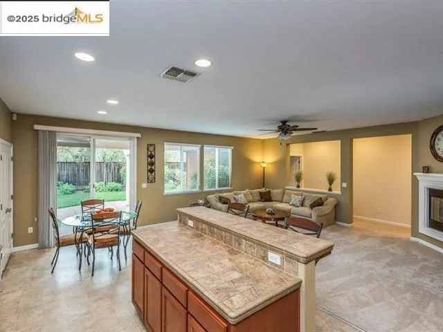 Kitchen with brown cabinets, recessed lighting, a glass covered fireplace, tile counters, and a center island