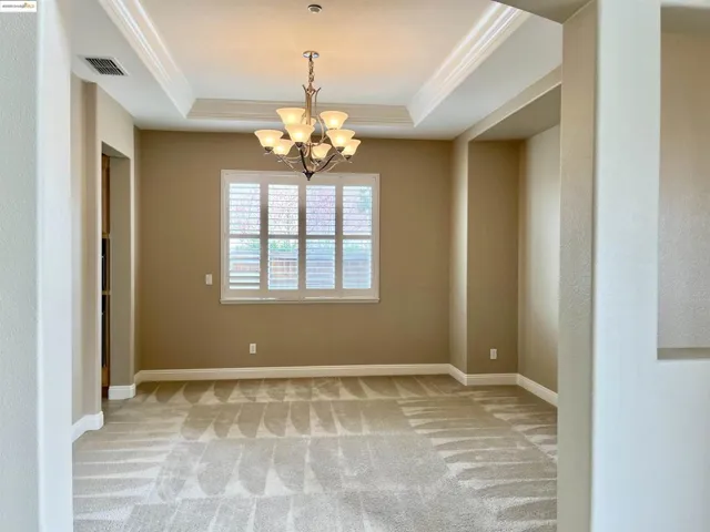 Spare room featuring a chandelier, light colored carpet, crown molding, and a raised ceiling