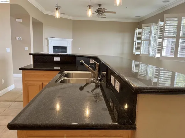 Kitchen featuring hanging light fixtures, ornamental molding, dark stone counters, a fireplace, and light brown cabinetry