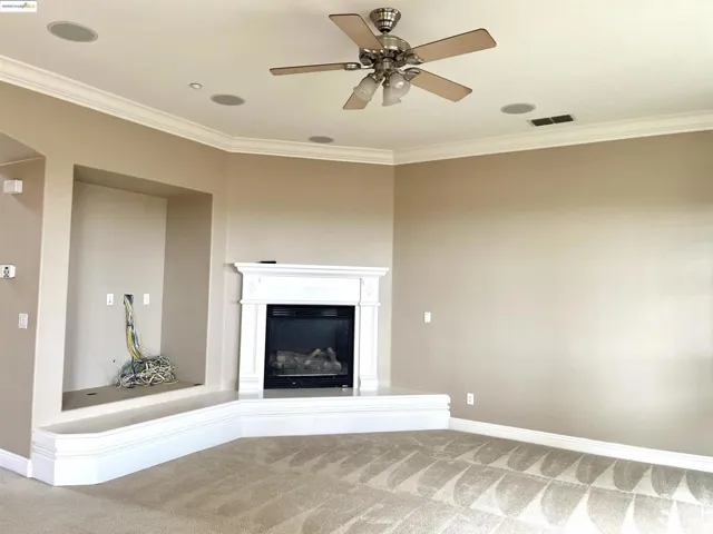 Unfurnished living room with carpet floors, crown molding, a glass covered fireplace, and a ceiling fan