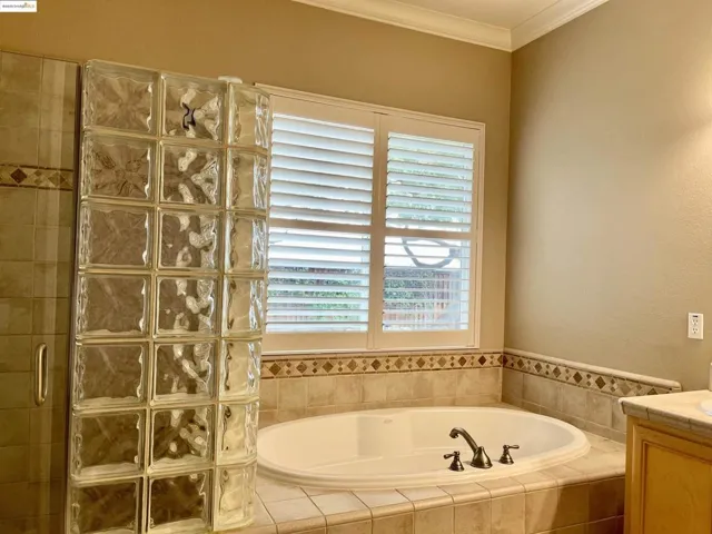 Bathroom featuring a garden tub, a tile shower, crown molding, and vanity