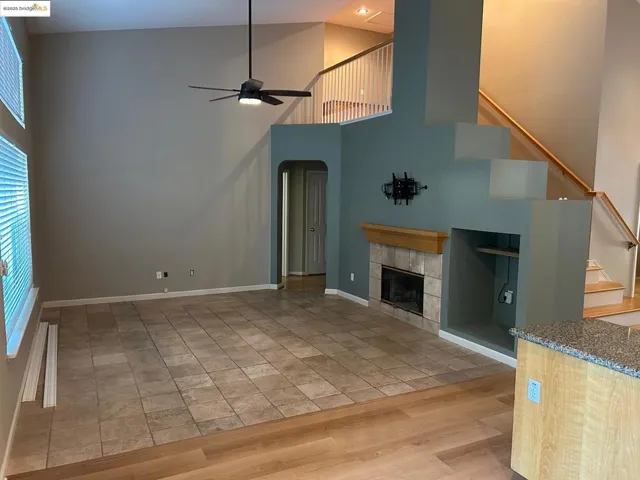 Unfurnished living room featuring a high ceiling, a fireplace, arched walkways, light wood-type flooring, and a ceiling fan