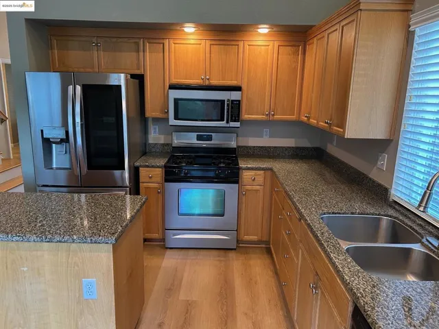 Kitchen with appliances with stainless steel finishes, light wood-type flooring, brown cabinets, and dark stone countertops