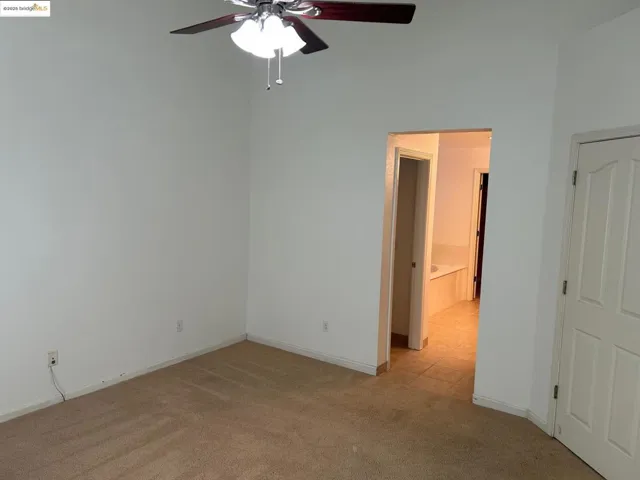 Unfurnished bedroom featuring light colored carpet, ensuite bath, and a ceiling fan