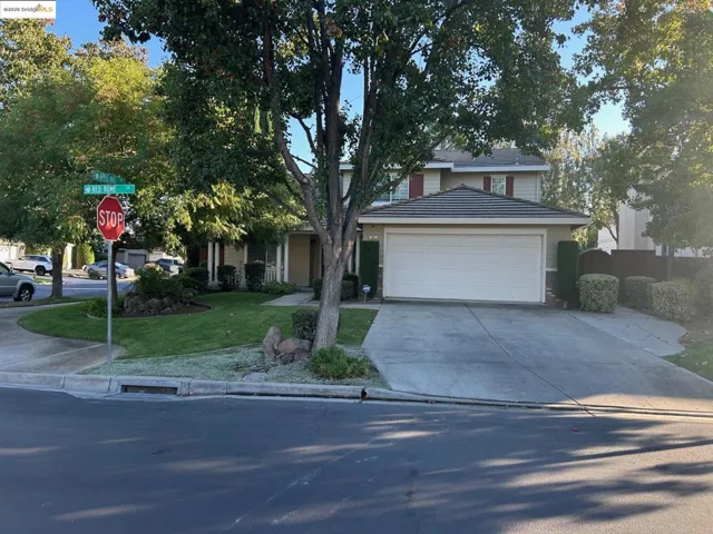 View of property hidden behind natural elements featuring concrete driveway, a front yard, and a garage