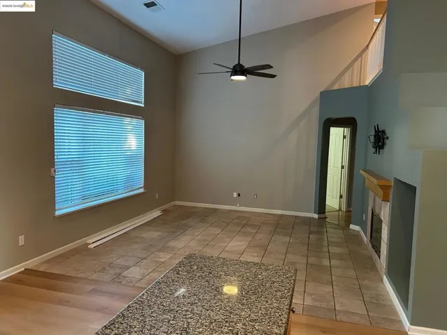 Unfurnished living room featuring a fireplace, a ceiling fan, arched walkways, a high ceiling, and light wood finished floors
