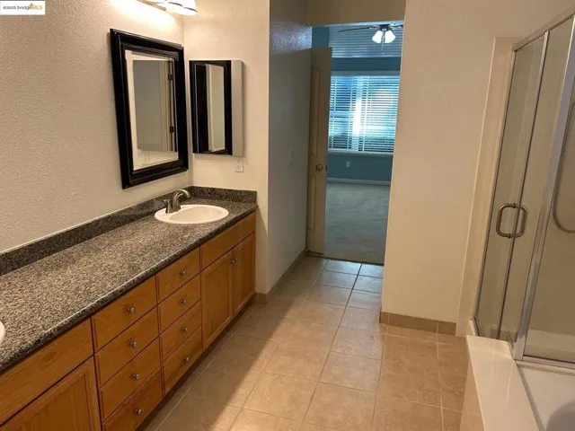 Bathroom with double vanity, a stall shower, light tile patterned flooring, and a textured wall