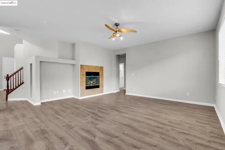Unfurnished living room with a tiled fireplace, light wood-type flooring, ceiling fan, and stairs