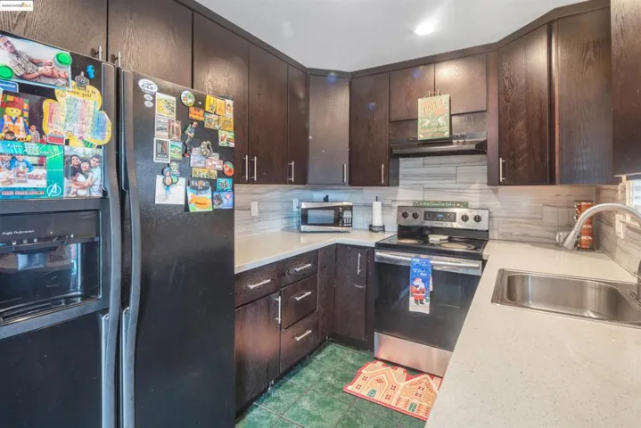 Kitchen featuring appliances with stainless steel finishes, dark brown cabinetry, tasteful backsplash, and under cabinet range hood