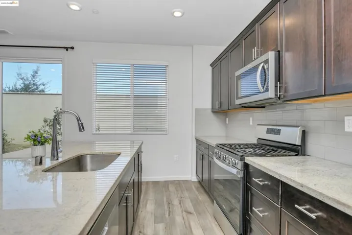 Kitchen with appliances with stainless steel finishes, light stone counters, light wood-type flooring, decorative backsplash, and recessed lighting