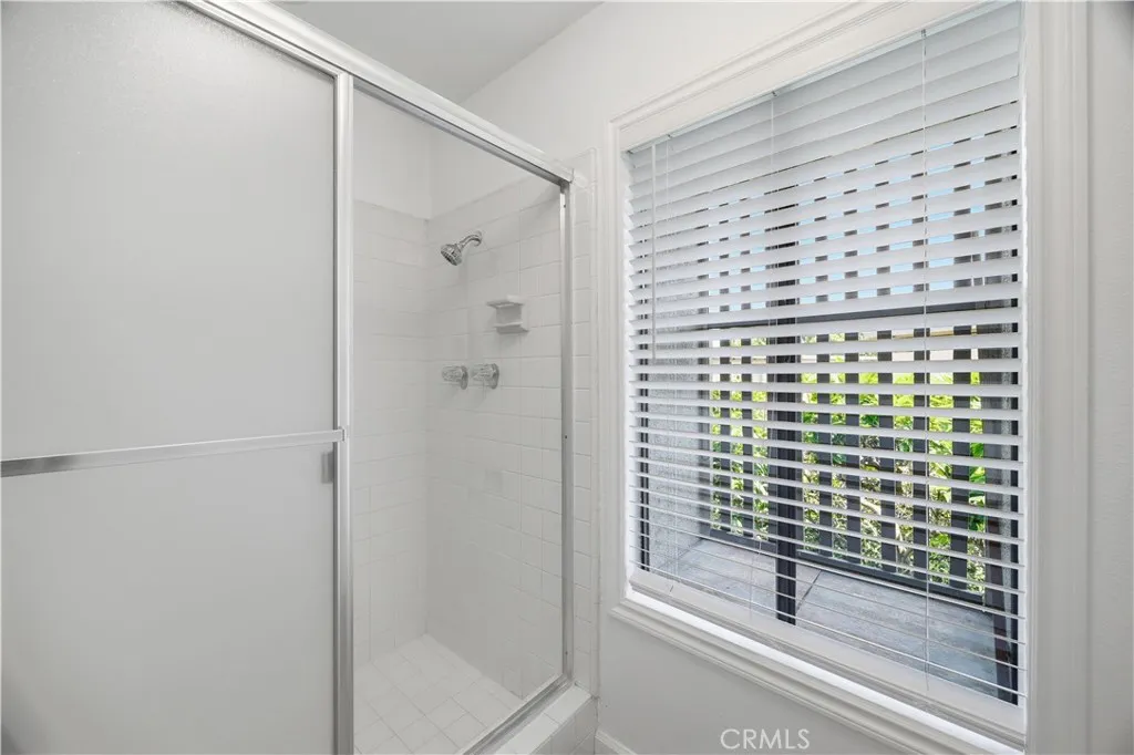 The walk-in shower in the primary bathroom with glass door closure and brand-new window blinds.