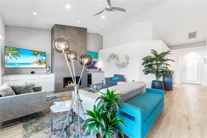 Striking ceiling-to-floor tiled fireplace anchors the space, featuring built-in cabinets with beverage refrigerator, vaulted ceilings, and elegant luxury vinyl plank flooring.