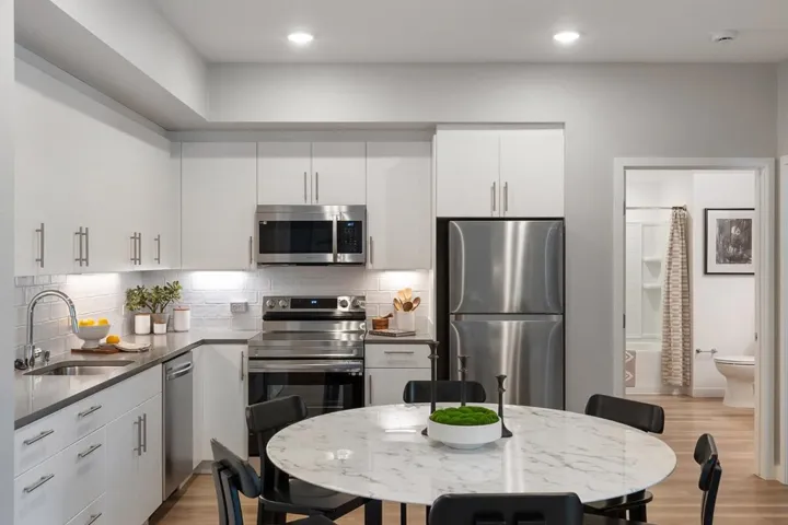 Kitchen featuring appliances with stainless steel finishes, backsplash, light wood-style flooring, white cabinetry, and dark stone counters