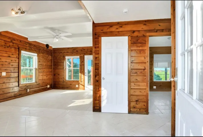 Spare room featuring wooden walls, tile patterned floors, a ceiling fan, and beamed ceiling