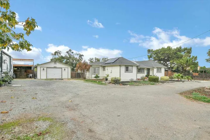 View of front of property with a garage, solar panels, an outdoor structure, and driveway