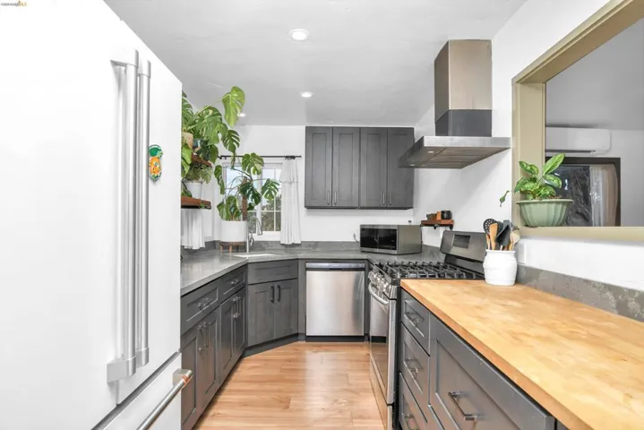 Kitchen with stainless steel appliances, wall chimney range hood, light wood finished floors, gray cabinets, and recessed lighting