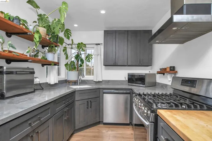Kitchen with open shelves, stainless steel appliances, ventilation hood, recessed lighting, and light wood-style flooring