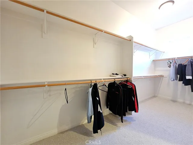Spacious walk-in closet attached to the primary suite, offering generous storage capacity and a functional layout. Features an L-shaped design with ample hanging rods and shelving to keep your wardrobe organized. The clean, neutral finishes, plush carpeting, and recessed lighting create a bright, inviting, and highly practical dressing area.